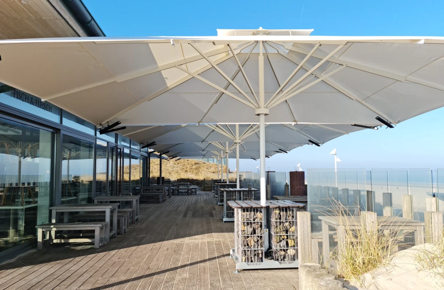 Terrasse mit großen Sonnenschirmen am Strand bei klarem Himmel